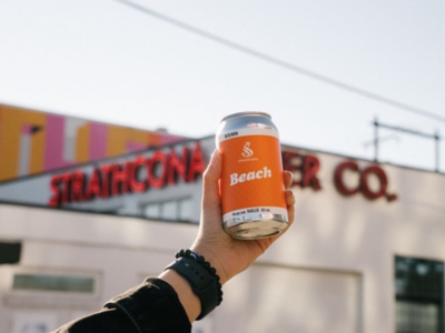 A raised can of Strathcona beach Radler in front of Strathcona Beer Company.